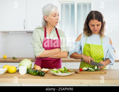 Madre anziana che insegna figlia adulta come cucinare insalata di verdure in cucina Foto Stock