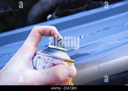 Una mano che utilizza una bomboletta spray per verniciare una superficie metallica automobilistica Foto Stock