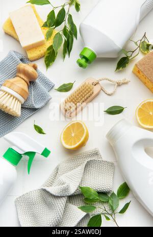 Prodotti per la pulizia naturali, fette di limone, spazzole e spugne disposte su una superficie bianca per una pulizia eco-consapevole Foto Stock