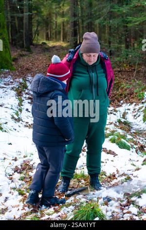 Un adulto e un bambino, vestiti in modo caldo, stanno vicino a un piccolo incendio in una foresta invernale innevata. Sembrano occuparsi del fuoco, godendosi un momento tranquillo in n Foto Stock
