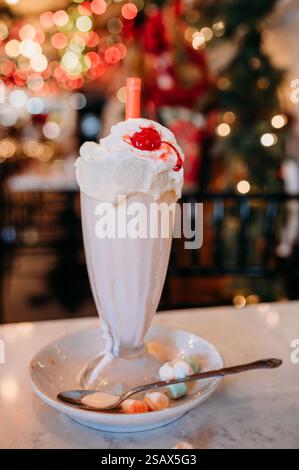Un frullato di latte che si scioglie con panna montata e ciliegia in una caffetteria festosa. Foto Stock