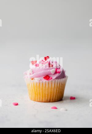 Primo piano del cupacke con glassa rosa e cuori su sfondo bianco. Foto Stock