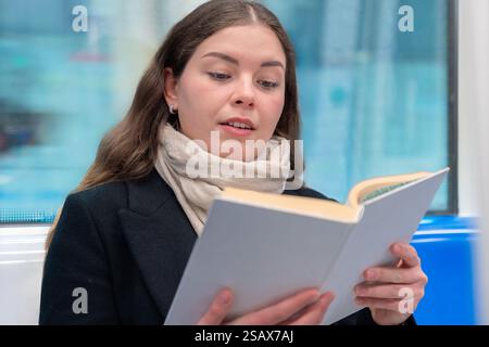 Giovane donna che legge un libro mentre viaggia su un treno della metropolitana Foto Stock
