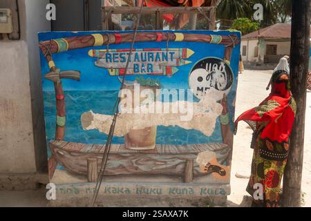Africa Tanzania, Zanzibar, costa orientale, Jambiani, villaggio, donna locale vestita in colori, accanto al murale del ristorante Foto Stock