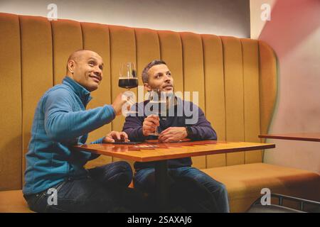 Due uomini si godono la birra artigianale in un bar accogliente Foto Stock