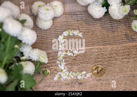 Fiori di crisantemo bianchi disposti a forma di simbolo della sterlina £ accanto a moneta da una sterlina d'oro posta su una superficie rustica in legno, sterlina, finanza Foto Stock