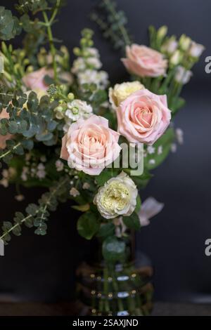 Una splendida composizione floreale caratterizzata da delicate rose rosa e lussureggianti foglie verdi, disposte in un elegante vaso di vetro. Perfetto per matrimoni Foto Stock