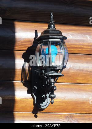 La lanterna decorativa per esterni è montata su una parete in legno con lampadina blu. Foto Stock