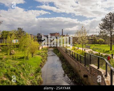 Il fiume Medlock scorre attraverso Mayfield Park, l'area Ardwick Green di Manchester in lontananza. Foto Stock
