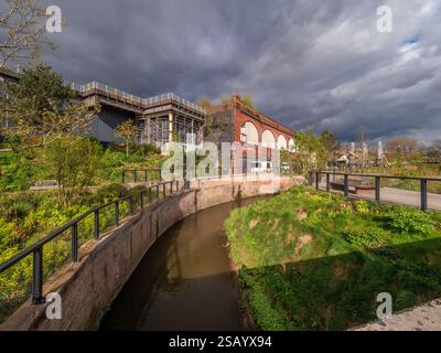 Il fiume Medlock scorre attraverso Mayfield Park con Depot Mayfield sulla sinistra e il parco giochi sulla destra. Foto Stock