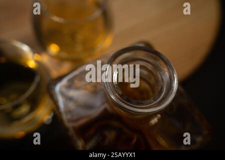 Primo piano di una bottiglia di whisky con due bicchieri, che mette in risalto le ricche tonalità di ambra e i riflessi eleganti Foto Stock