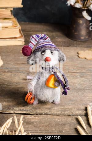 Giocattolo lavorato a mano - un topo grigio in un cappello con formaggio su fondo di legno. Giocattoli interni a uncinetto. Foto Stock