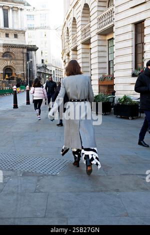 Vista posteriore della donna anziana che indossa un elegante cappotto di lana con cintura nera borchiata, quartiere finanziario Londra Inghilterra Regno Unito 2025 KATHY DEWITT Foto Stock