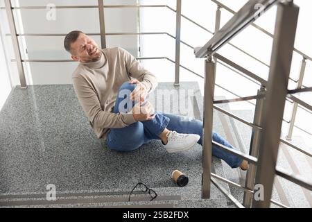 Uomo con un ginocchio ferito sulle scale dell'edificio dopo la caduta. Incidente pericoloso Foto Stock