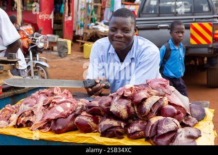 Macellaio con carne fresca in vendita in uno stand in un mercato all'aperto nell'Uganda rurale. Foto Stock