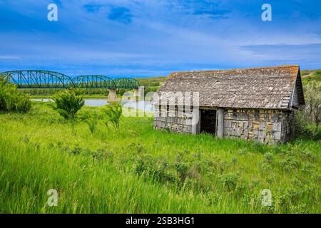 Una piccola casa è in un campo vicino a un fiume. La casa è fatta di legno e ha un tetto di paglia Foto Stock