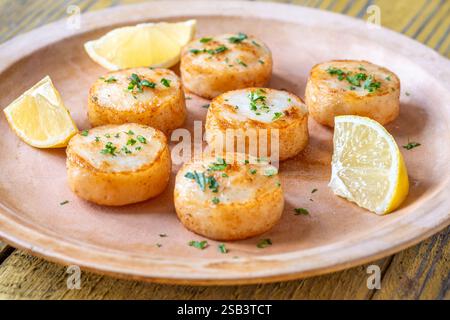 Morbide capesante fritte in burro servite con limone, prezzemolo, rustico fondo giallo Foto Stock