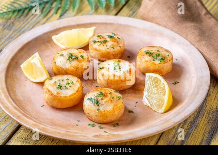 Morbide capesante fritte in burro servite con limone, prezzemolo, rustico fondo giallo Foto Stock