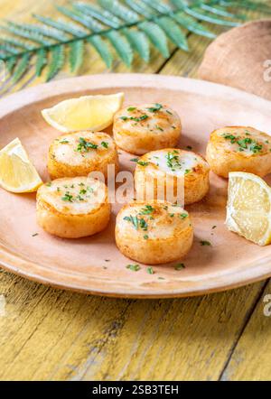 Morbide capesante fritte in burro servite con limone, prezzemolo, rustico fondo giallo Foto Stock