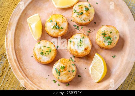 Morbide capesante fritte in burro servite con limone, prezzemolo, rustico fondo giallo Foto Stock
