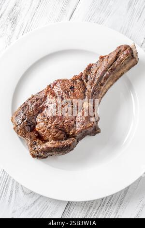 Bistecca di cowboy di media rara grigliata servita su un piatto bianco su un tavolo di legno bianco Foto Stock