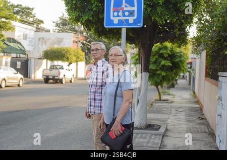 Una coppia anziana in piedi alla fermata dell'autobus che aspetta. Foto Stock
