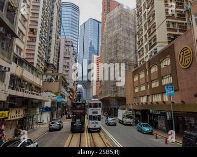 Hong Kong, Cina - 1 febbraio 2025: Un classico tram di Hong Kong scivola lungo una strada stretta, fiancheggiata da edifici torreggianti, vecchi e nuovi, che mostrano t Foto Stock