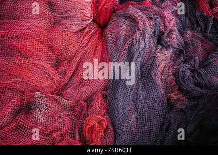 Primo piano dettagliato di vivaci reti da pesca rosse e nere impilate insieme, che mostrano intricati motivi a rete e colori contrastanti. La consistenza usurata AN Foto Stock
