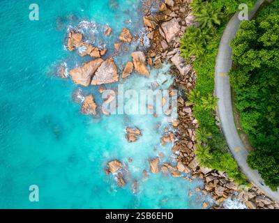 Vista aerea della costa dell'isola di la Digue, Seychelles, che mostra acque turchesi, grandi massi sparsi, una strada tortuosa costeggiata da verde lussureggiante Foto Stock