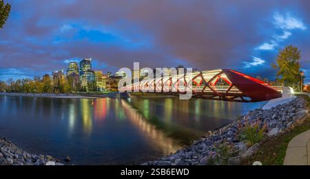 Una vista panoramica del Ponte della Pace a Calgary, Canada, al crepuscolo. Il ponte pedonale rosso attraversa il fiume Bow, con il moderno skyline della città Foto Stock