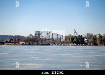 WASHINGTON DC - Un bacino di marea ghiacciato è visto in un giorno d'inverno, con lo skyline di Rosslyn, Virginia, visibile sullo sfondo. Gli alberi dormienti lungo la riva si stagliano in contrasto con la loro apparizione durante l'annuale National Cherry Blossom Festival in primavera. Le attrezzature da costruzione sono visibili lungo la banchina. Foto Stock
