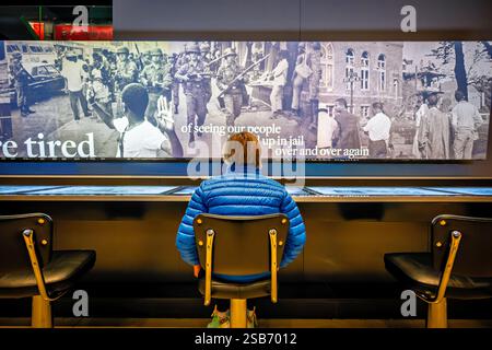 Greensboro Sit-Ins Exhibit National Museum of African American History a Washington DC | WASHINGTON D.C., Stati Uniti - Un visitatore si siede davanti a un montaggio a parete di fotografie dell'epoca dei diritti civili presso il National Museum of African American History and Culture, parte di una mostra interattiva sulla segregazione e la resistenza nel Sud americano. La stazione touchscreen consente ai visitatori di esplorare le immagini d'archivio e le testimonianze dell'epoca, comprese le scene delle truppe della Guardia Nazionale schierate durante i disordini degli anni '1960. La mostra ospita le gallerie sotterranee di storia del museo. Foto Stock