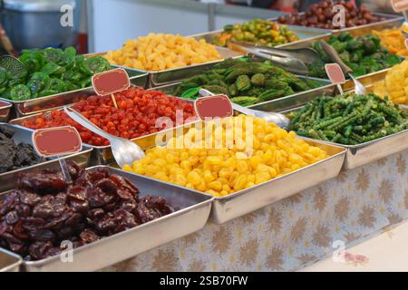 Vivace assortimento di frutta candita tailandese esposto in vassoi in acciaio inox presso un mercato locale. Questa selezione colorata include conservate e candite Foto Stock