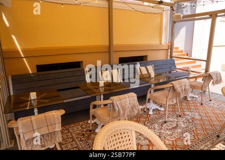 Un accogliente patio da caffe' adornato con sedie in vimini e vegetazione lussureggiante, a creare un'atmosfera serena. L'interno presenta un primo piano di chicchi di caffè in un gr Foto Stock