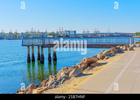 Long Beach, California - 15 gennaio 2025: Vista di un molo di legno che si estende sulle acque calme di Long Beach, con gru industriali e un ponte nel Foto Stock