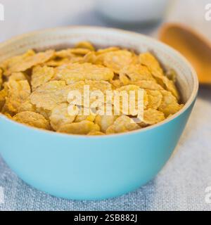Granoturco croccante non zuccherato in ciotola blu, latte e cucchiaio sul retro, fotografati con luce naturale (messa a fuoco selettiva) Foto Stock
