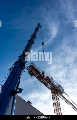 Costruzione di una gru da costruzione utilizzando una gru mobile. Ripresa diurna di entrambe le macchine contro un cielo blu Foto Stock