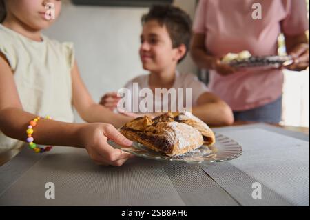 Due bambini seduti a un tavolo in un'accogliente sala da pranzo, in procinto di gustare dolci appena sfornati serviti su un piatto di vetro sotto la luce naturale, showca Foto Stock