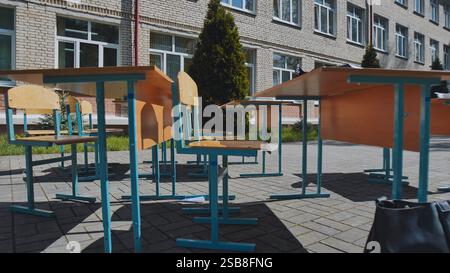 Le scrivanie e le sedie vuote si trovano all'esterno di un edificio scolastico in una giornata di sole, suggerendo una lezione all'aperto o una pausa Foto Stock