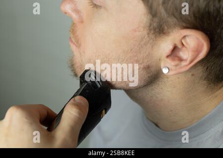 l'uomo rifinisce la barba con un rifinitore. Primo piano. Un rasoio elettrico per rifinire la barba. Cura della barba a casa. Foto Stock