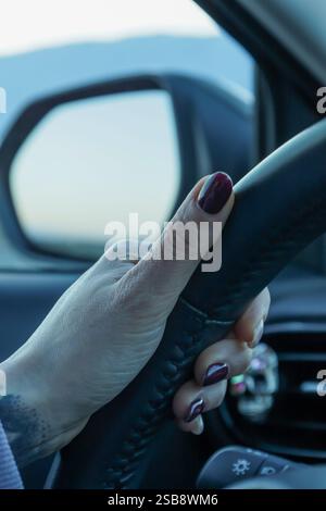 Primo piano di una mano con smalto viola scuro che afferra il volante di un'auto. Atene Grecia - 15 gennaio 2025 Foto Stock