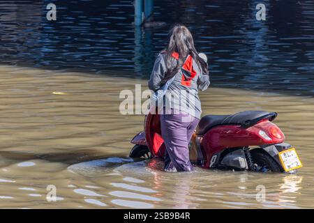 Una donna spinge una moto attraverso una strada allagata, la Thailandia Foto Stock