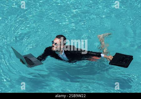 Affari estivi pazzi. Stile di vita di lavoro divertente. Bel uomo d'affari in tuta che usa un computer portatile in piscina. Uomo d'affari divertente. Concetto di freelance Foto Stock