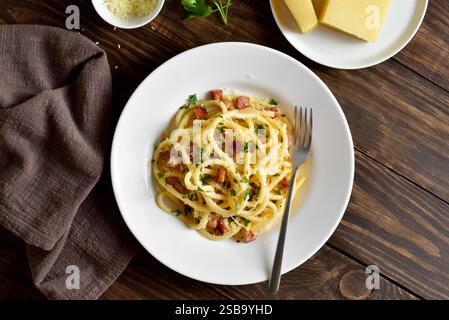 Pasta alla Carbonara, spaghetti con pancetta croccante e pepe nero su piatto bianco su fondo in legno. Cucina tradizionale italiana. Vista dall'alto, disposizione piatta Foto Stock