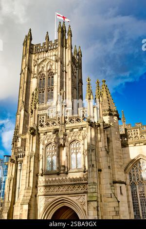 Una vista ravvicinata di una parte della Cattedrale di Manchester, che mostra le sue intricate opere in pietra, le alte guglie, le finestre ad arco e una bandiera in cima alle agains della torre Foto Stock