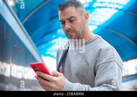 Uomo che usa lo smartphone rosso alla stazione ferroviaria Foto Stock