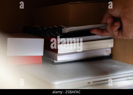 Una mano che cerca un notebook su uno scaffale pieno di libri e un notebook. Foto Stock