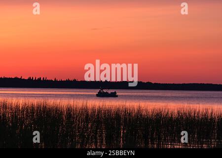 Una barca galleggia su un lago al tramonto. Il cielo è un bel mix di sfumature rosa e arancio Foto Stock