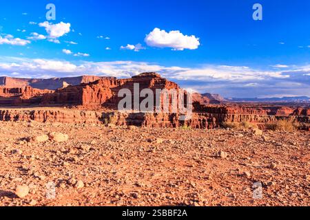 Un paesaggio desertico con una grande formazione rocciosa sullo sfondo. Il cielo è limpido e blu, e il sole splende brillantemente. La scena è pacifica Foto Stock