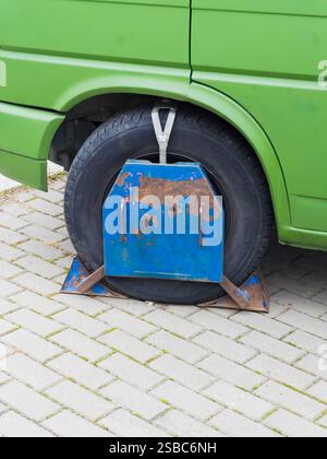 Primo piano di un furgone verde bloccato con un morsetto in metallo arrugginito e blu a causa di un parcheggio illegale. Foto Stock